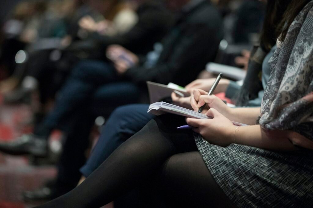Close-up of attentive audience members taking notes at a workplace lecture.