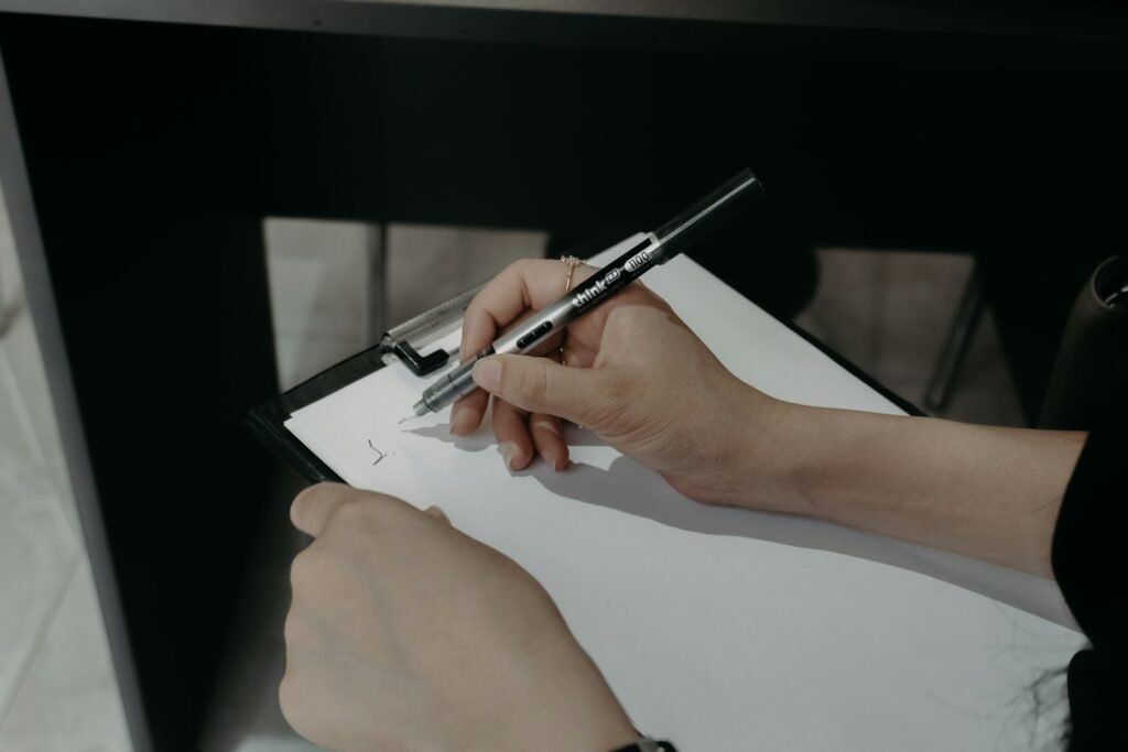 Hands writing on a clipboard with a pen.
